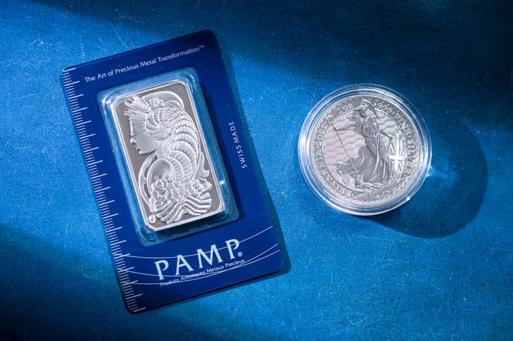 pexels photo 20979924 Close-up of a silver coin and a PAMP bar on a blue textured background emphasizing wealth.