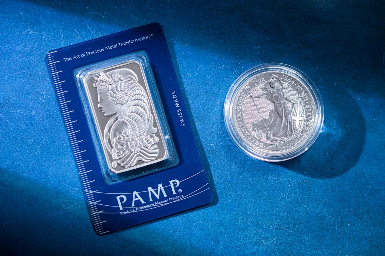 services-04 Close-up of a silver coin and a PAMP bar on a blue textured background emphasizing wealth.